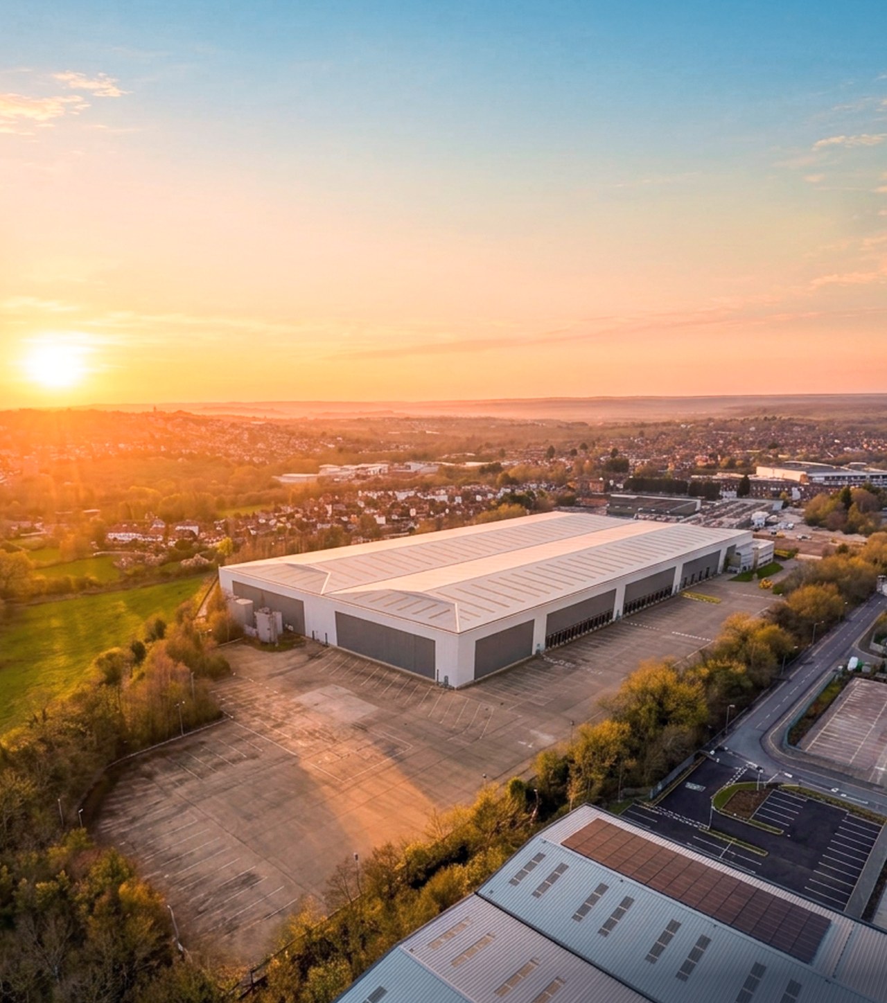 Langley 255 from the air at sunrise: a large white distribution unit with a broad concrete yard, among trees on the edge of Langley Mill
