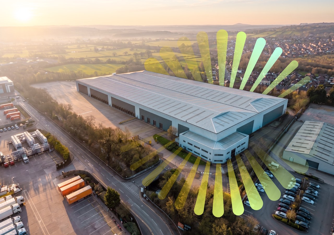 Langley 255 from the air at golden hour: the long warehouse with its dock doors along one side and the two-storey office block at the near corner, with the Sunrise rays fanning out behind the building